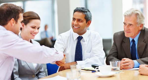 Four business people in a meeting, two shaking hands
